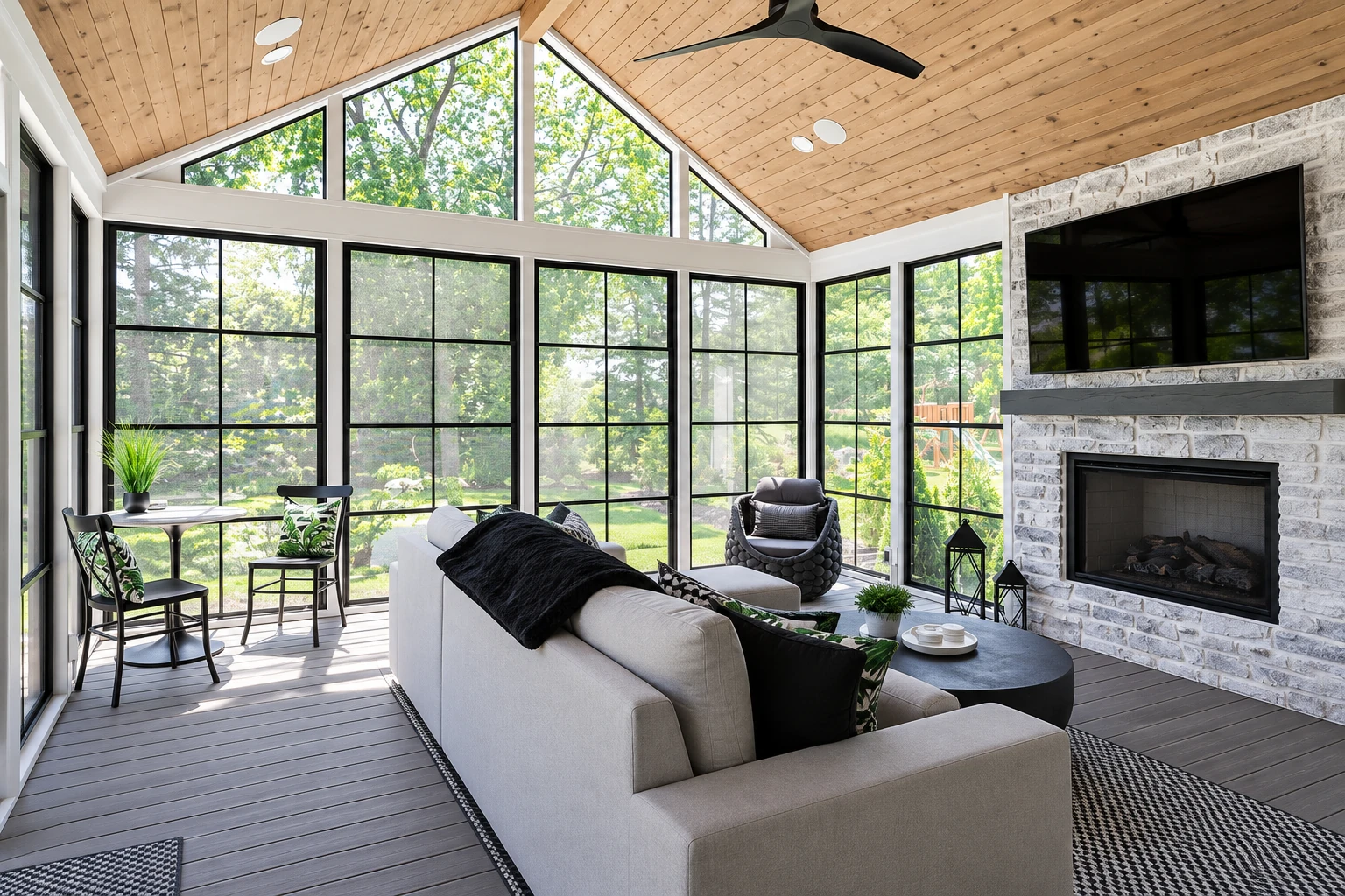All-season sunroom with tall black-framed windows, a vaulted wood ceiling, white sofa, and stone fireplace.