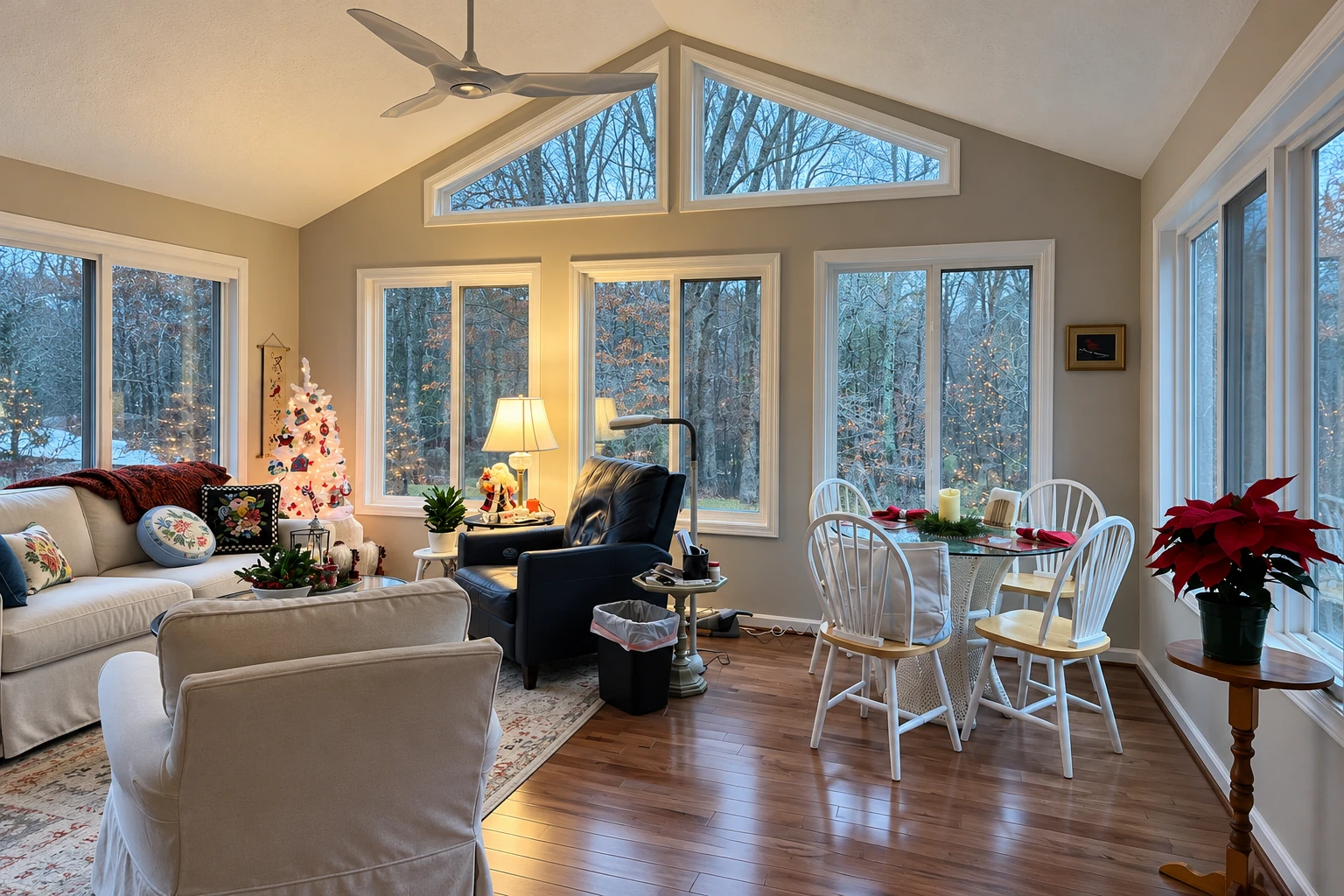 A four-season sunroom with tall windows, a peaked ceiling, a ceiling fan, and a cozy seating and dining area.