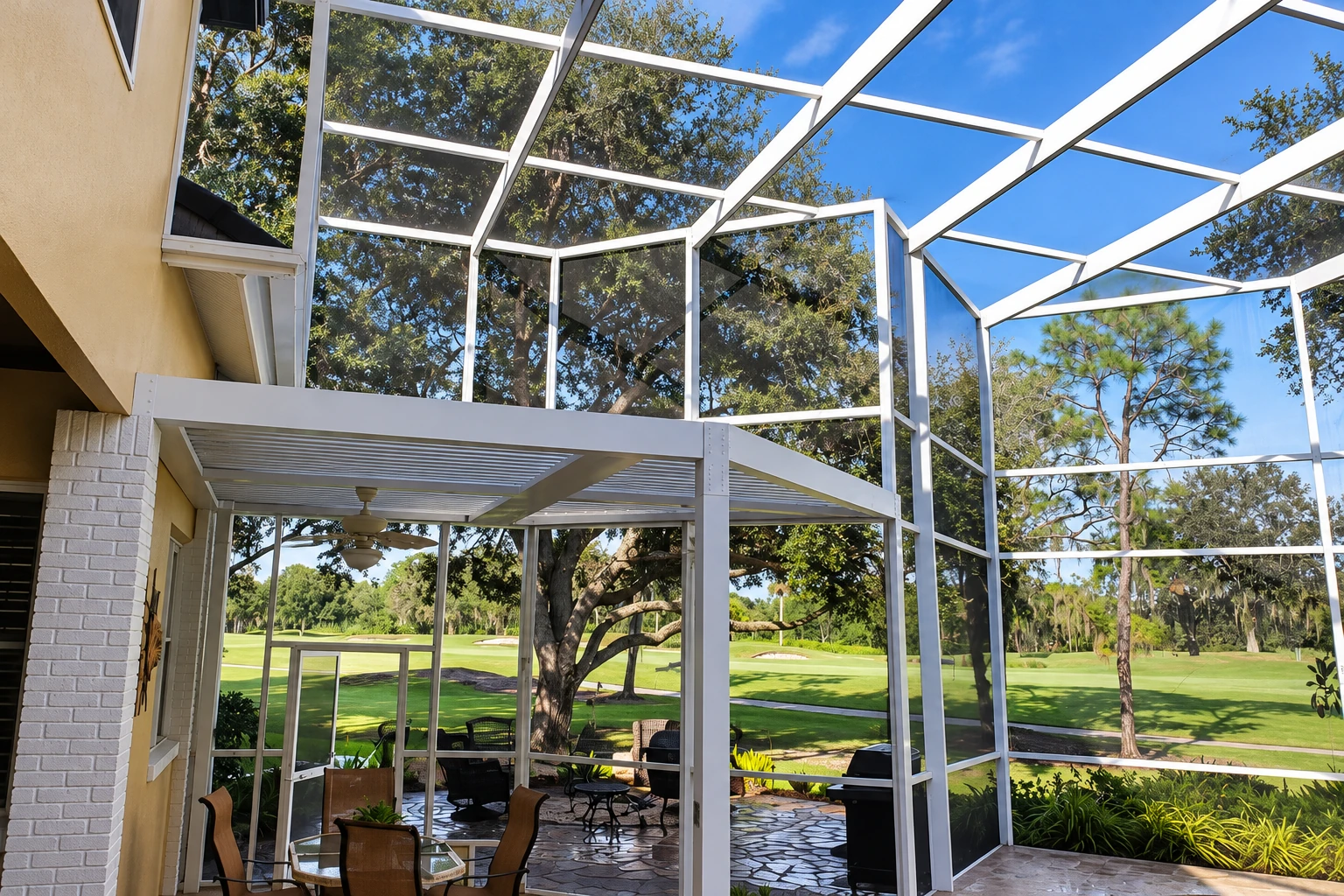 A screened patio enclosure has a white roof frame and mesh walls overlooking a green lawn and trees.