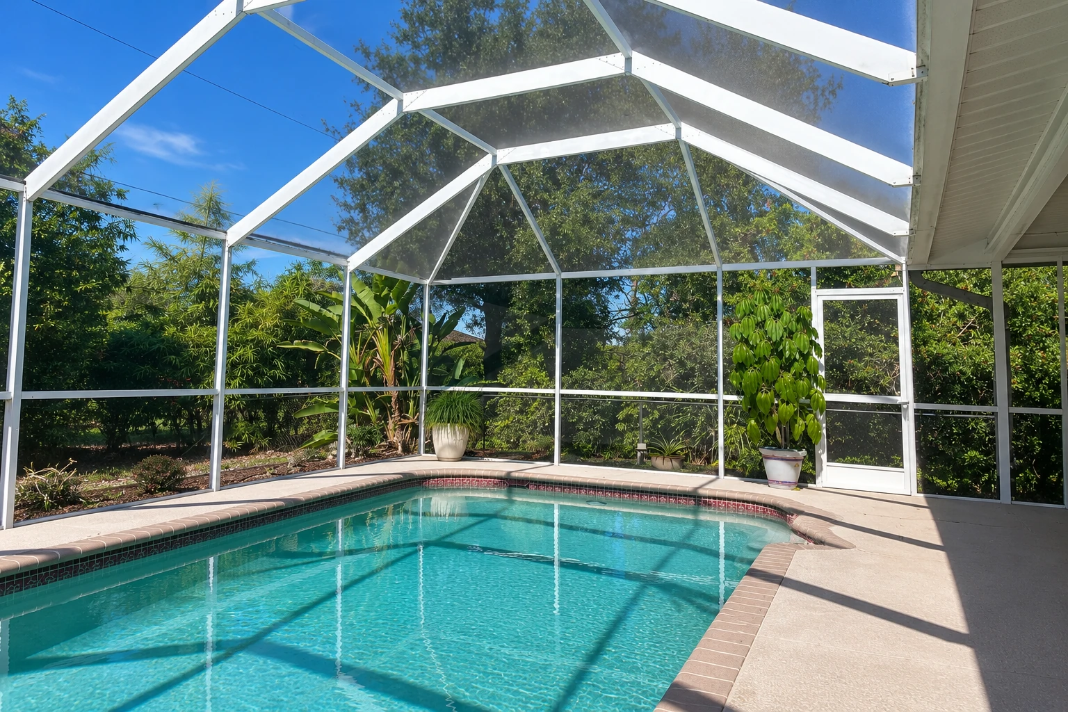 A screened patio enclosure surrounds a turquoise swimming pool, with white framing and leafy garden views.