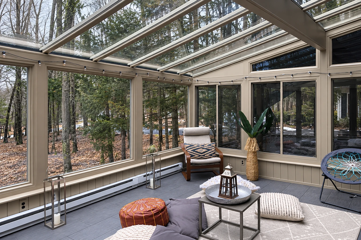 Solarium with a glass roof and walls, neutral framing, and casual seating overlooking a wooded yard.