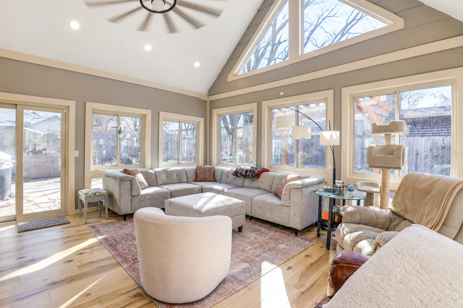 Bright sunroom living room with a vaulted ceiling, large windows, and a sectional sofa around a patterned rug.